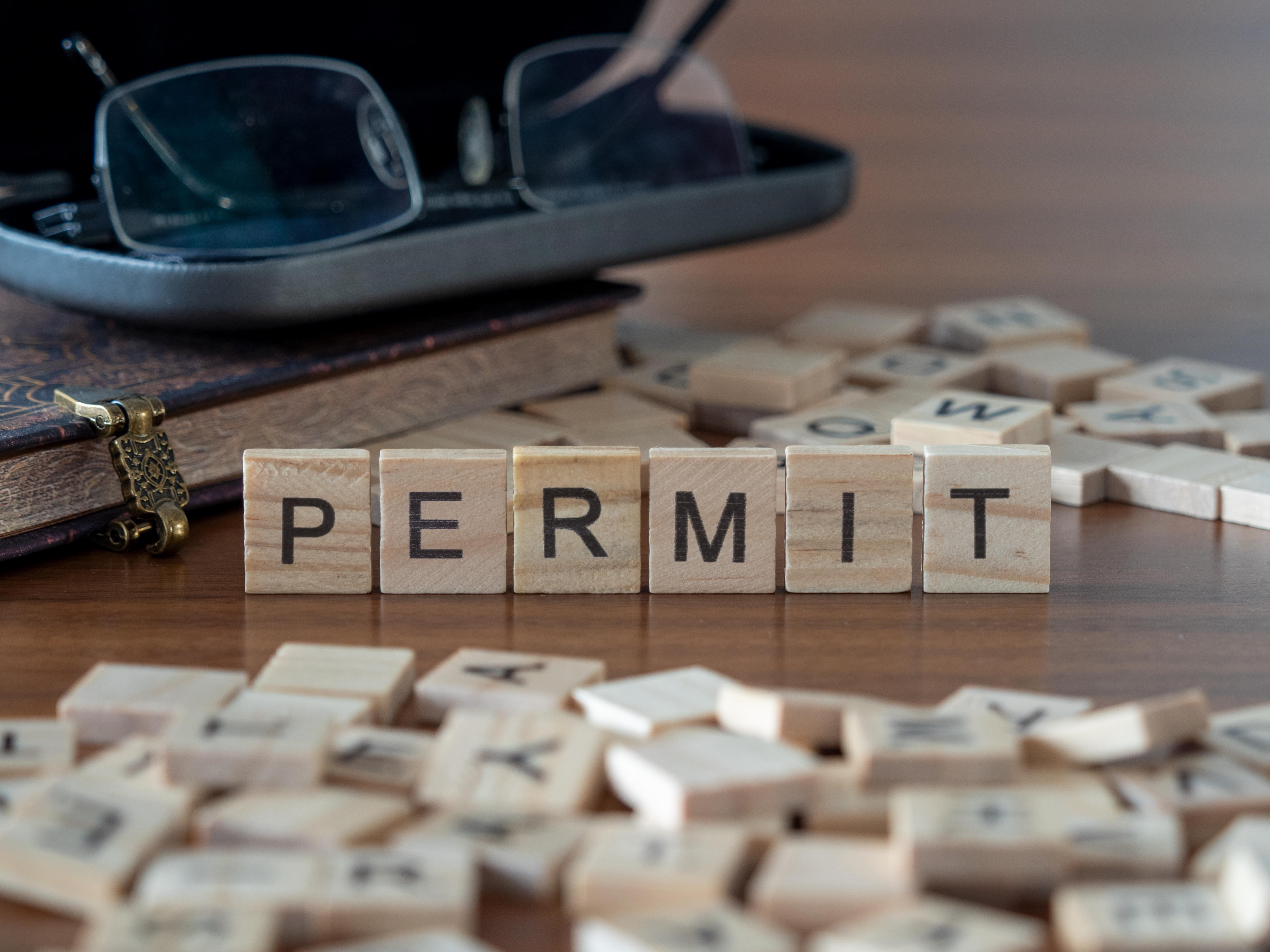 permit word or concept represented by wooden letter tiles on a wooden table with glasses and a book von lexiconimages