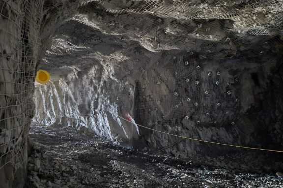 The image depicts an underground tunnel with rough, unstable rock formations and exposed cables. Le contenu généré par l'IA peut être incorrect.
