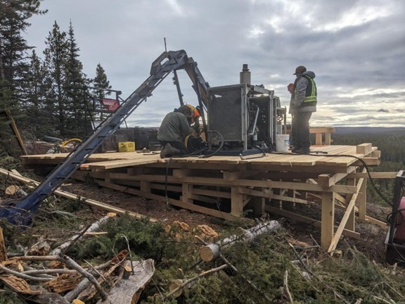 The image shows a construction worker operating a bulldozer next to a partially completed wooden structure, surrounded by trees and under a cloudy sky.<br /> <br /> AI-generated content may be incorrect.