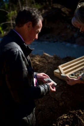 A person is holding a shovel while standing near a pile of dirt and a wooden structure.<br /> <br /> AI-generated content may be incorrect.