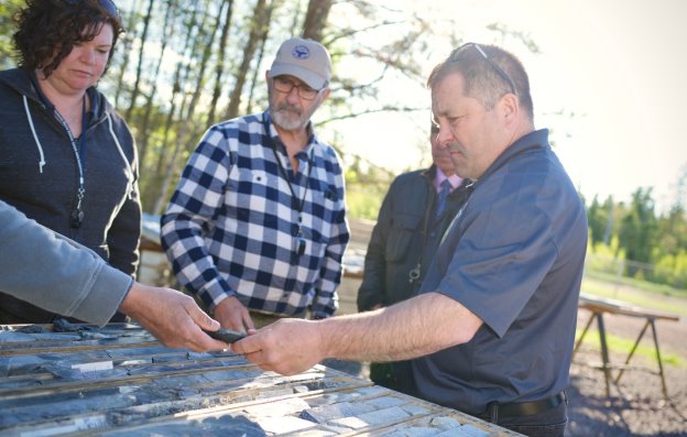 Three people are engaged in a hands-on activity, possibly measuring or laying down materials, outdoors under a clear sky.<br /> <br /> AI-generated content may be incorrect.