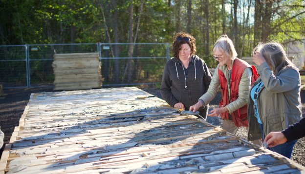 The image shows a group of people standing around a construction site, possibly working on a wooden structure.<br /> <br /> AI-generated content may be incorrect.