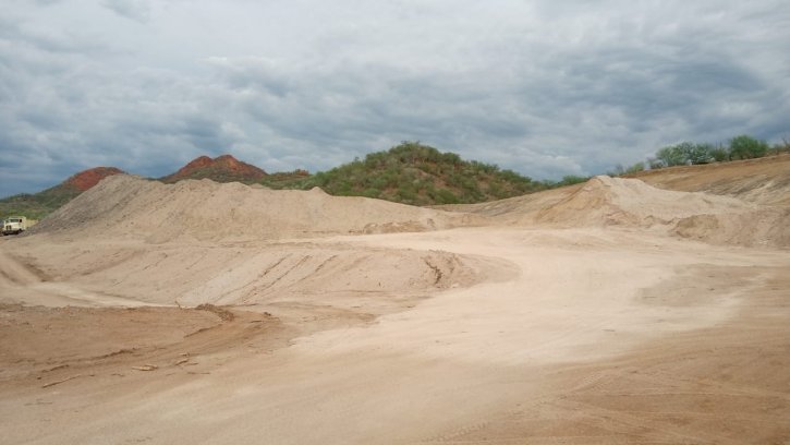 The image depicts a barren, unpaved, and uneven terrain with a landscape of red, orange, and brown mounds, under a cloudy, overcast sky.<br /> <br /> AI-generated content may be incorrect.