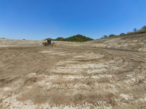 The image depicts a large, unpaved construction site with a bulldozer in the foreground, under a clear blue sky. AI-generated content may be incorrect.