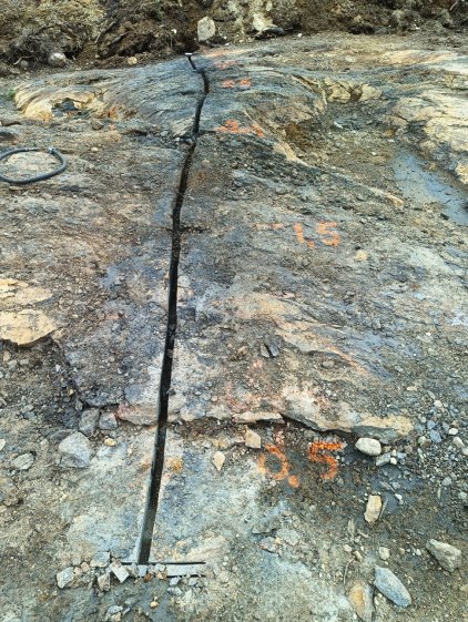 The image shows a weathered, cracked rock surface with visible markings and a partially exposed, uneven ground. AI-generated content may be incorrect.